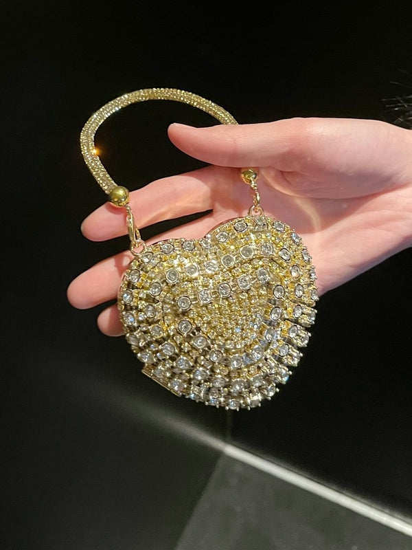 Hand holding a round, embellished clutch bag with a gold handle against a dark background