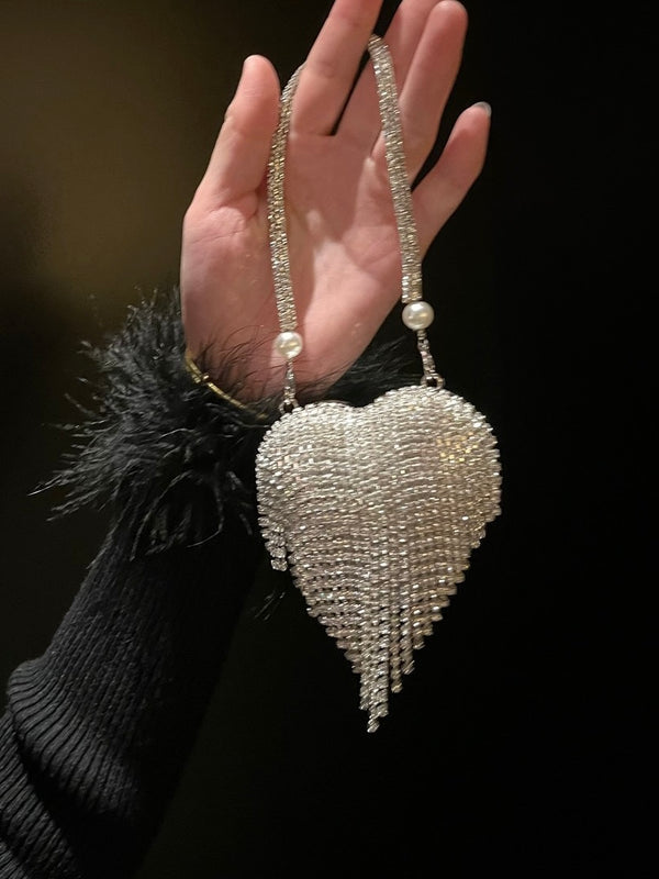 Hand holding a sparkling heart-shaped tassel mini bag against a dark background